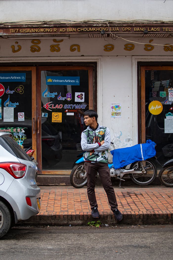 Young man leaning on a bike outside a travel agency in Laos, with urban street elements.